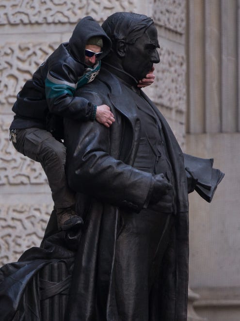 A fan climbs the John Wanamaker statue outside City Hall.