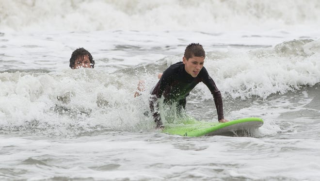 Robert Hurley prepares to pop up on a surf board after a receiving a push from instructor Wyatt Harrison in Ocean City on Sunday, Oct. 15, 2017.