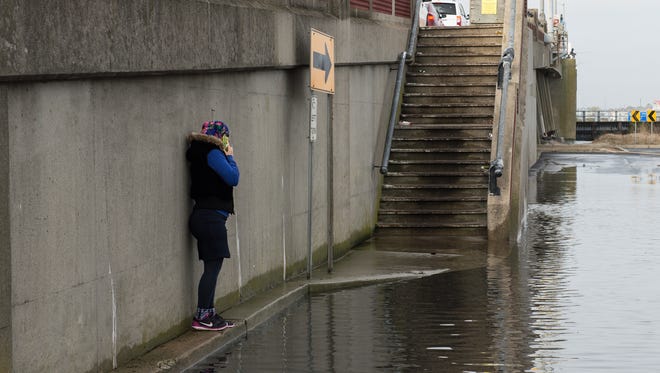 A women walks along a narrow curb in an attempt to avoid walking through a flooded section of North Division Street and Saint Louis Avenue in Ocean City on Sunday, Nov. 5, 2017.