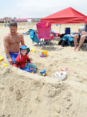 Mark Carnegie from Albany, New York with his grandson Spencer, 3, and family, work in the sand on Rehoboth Beach with their tent set up for protection from the sun.