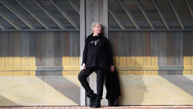 Ellen Roney Hughes wears a Black Pure Handknit cowl neck sweater; black slim-cut Calvin Klein pants, black Eileen Fisher velvet duster; Uggs boot;  and a necklace of black and silver cloth leaves.