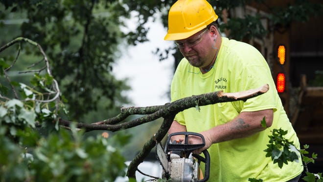 A worker uses a chainsaw cut tree branches that have fallen onto the street.