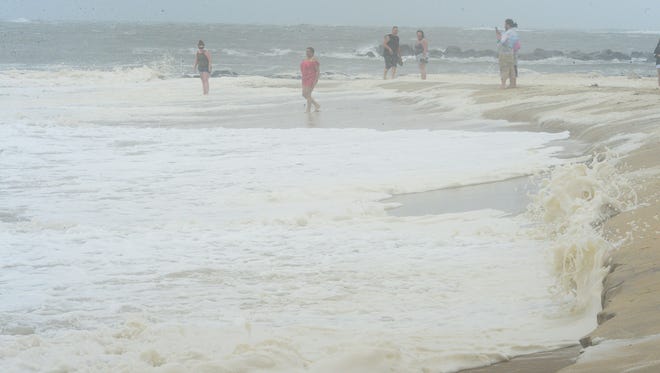 People walk the beach to look at the large waves on the beach in Ocean City where a summer nor'easter is passing through causing high winds, large waves and beach erosion on Saturday, July 29, 2017.