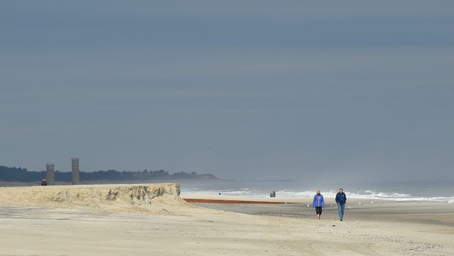 A couple walks next to a sand cliff that formed from the latest nor'easter that hit Rehoboth Beach.