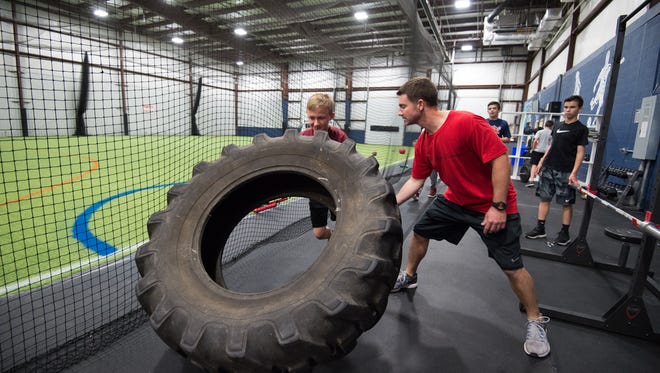 Jeff Simpson, right, owner and head strength coach with Sports Specific Training, helps Carter Boyd (12) flip over a tire during a training session at Slim's Sport Complex in Middletown.