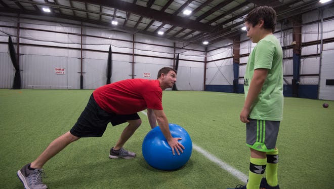 Jeff Simpson, left, owner and head strength coach with Sports Specific Training, demonstrates a push-up method using a ball to Aidan Quintana, at Slim's Sport Complex in Middletown.
