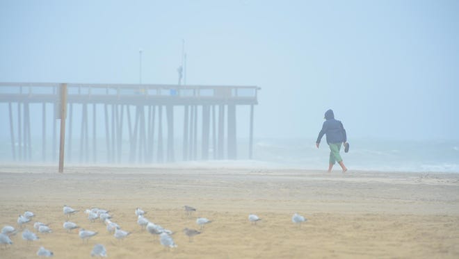 A woman walks across the beach in Ocean City, Md. as Hurricane Maria is off the coast in the Atlantic Ocean on Wednesday, Sept. 27, 2017.