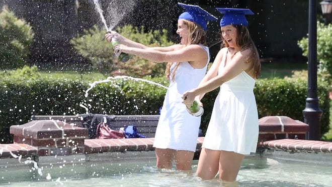 University of Delaware graduates pop bubbly for a souvenir photo in a campus fountain on the South Green Wednesday. The fountain is a popular spot for photos and dips for graduates - both during sanctioned periods this week and late night, illicit drop-ins.