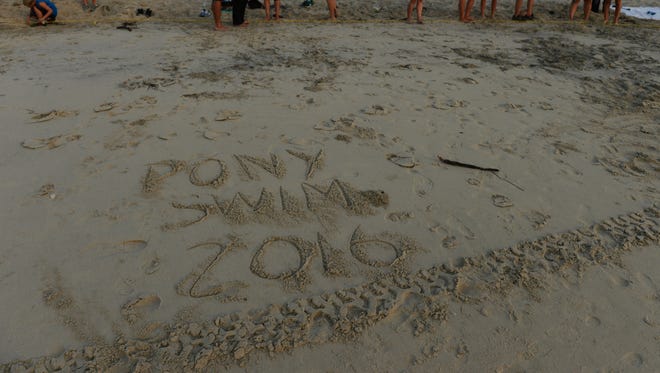Spectators watch near the words "PONY SWIM 2016" written in the sand as the northern herd of Chincoteague Ponies are led down the beach to their corral on Assateague Island, Va. on Monday morning, July 25, 2016. The 91st Annual Chincoteague Pony Swim is Wednesday.
