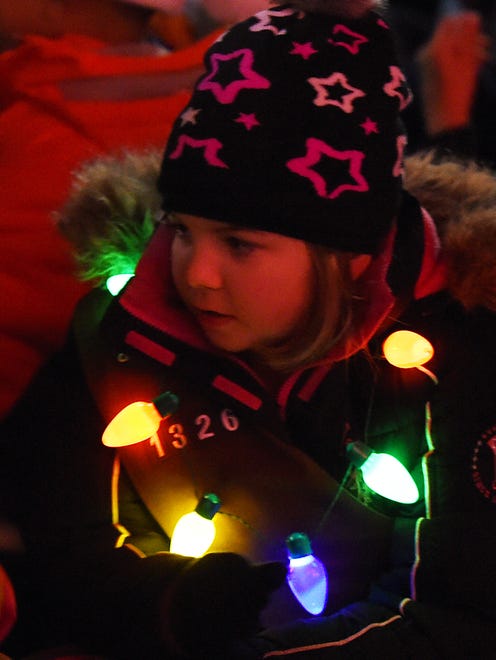 A young caroler is framed by lights.