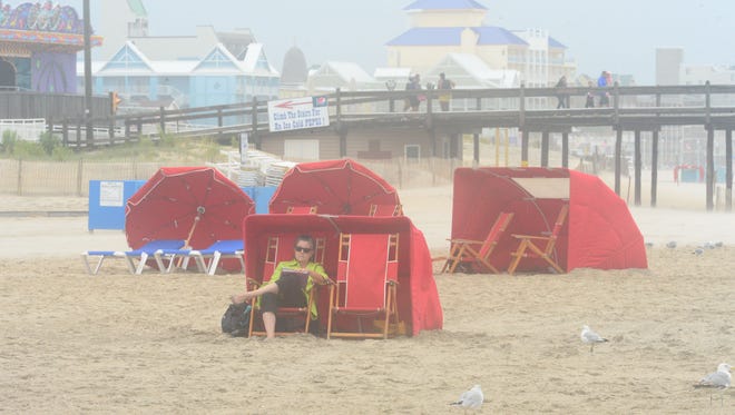 A woman reads a book as her back is to the high winds that are occurring in Ocean City, Md. from the summer nor'easter passing through on Saturday, July 29, 2017.