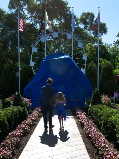 Sculptor Brian P. Hanlon takes his daughter May up for a closer look at the wrapped monument before unveiling gets underway. Unveiling of Welcome To Ocean County Monument on August 14, 2014 in Toms River. Monument represents all the residents of Ocean County and was created by sculptor Brian P. Hanlon and donated by the Jay & Linda Grunin Foundation.  - Peter Ackerman / Staff Photographer