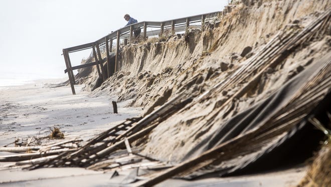 A woman peeks over the edge as the weekend storm caused damage to the dunes allow South Bethany beach where debris is scattered throughout the area.