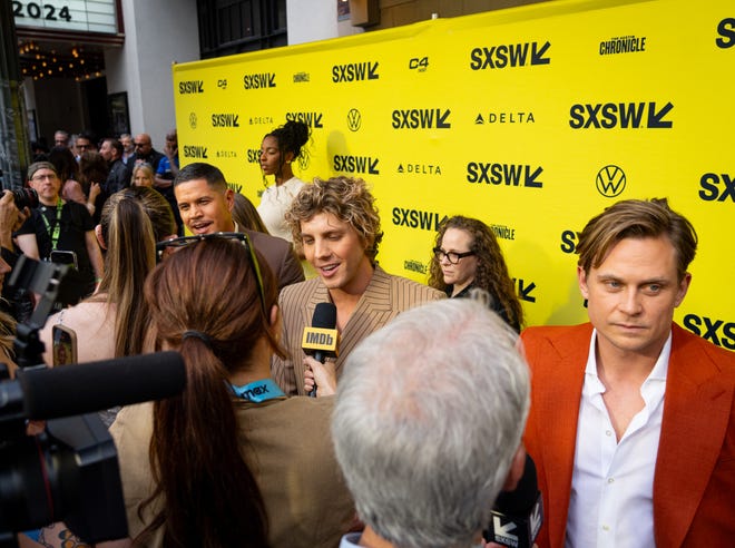 Billy Magnussen, right, and Lukas Gage, center, speak to the press on the red carpet before the premiere of Road House at the Paramount Theatre in Austin, Texas on the first day of South by Southwest, Friday, March 8, 2024. Magnussen plays the character "Ben Brandt" while Gage plays "Billy" in the movie.