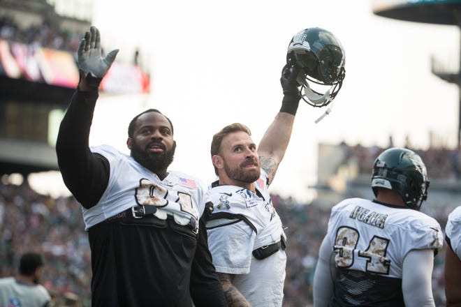 The Eagles' Fletcher Cox, left, and Chris Long wave to fans as they take the field for the first public practice of the season Sunday at Lincoln Financial Field.