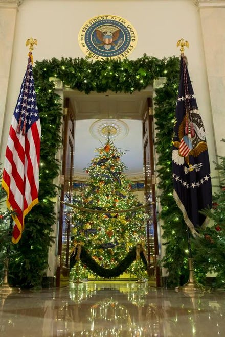 The Presidential seal is seen above an entrance to the Blue Room where the official White House Christmas tree is dressed in blue velvet ribbon embroidered in gold; as seen from the Cross Hall during a viewing of the 2018 holiday decorations at the White House in Washington, D.C.