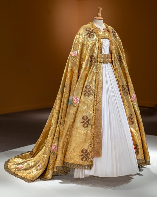 Michele Clapton's Imperial Mantle, decorated with symbols important to the of the British empire, is shown over a white pleated dress.